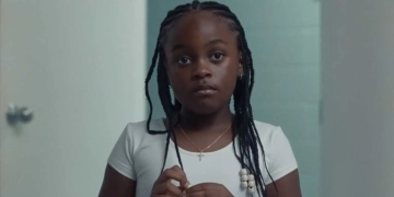 Gambar dari film On a Sunday at Eleven, tampak seorang anak berkulit hitam mengenakan kaos putih.